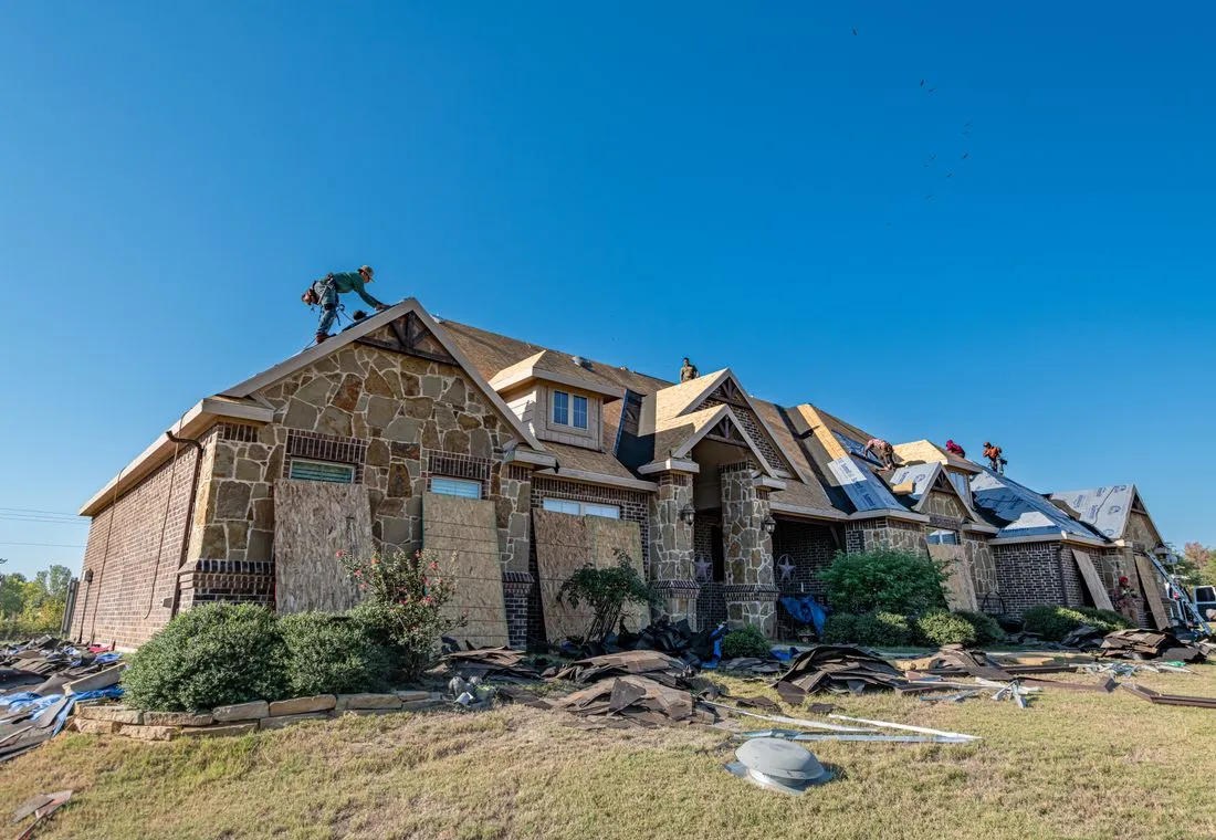 Roofing crew installing a new shingle roof on a Texas brick home under a clear sky