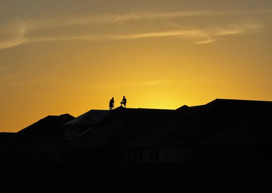 Roofing workers silhouetted on a rooftop against a Texas sunset sky